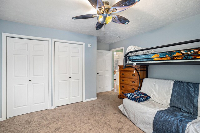 bedroom with light carpet, a textured ceiling, two closets, and ceiling fan