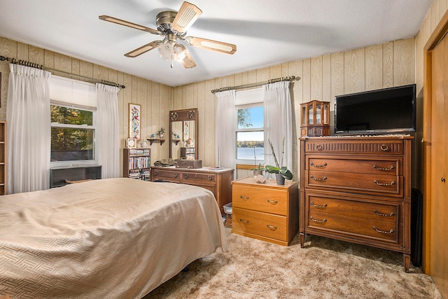 bedroom with multiple windows, wood walls, carpet, and ceiling fan