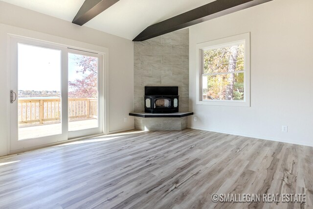 unfurnished living room with lofted ceiling with beams, light hardwood / wood-style floors, a wood stove, and plenty of natural light