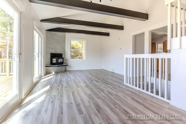 unfurnished living room with light hardwood / wood-style floors, a wood stove, and vaulted ceiling with beams