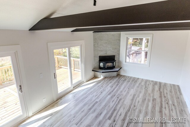 unfurnished living room with a wealth of natural light, light hardwood / wood-style floors, vaulted ceiling with beams, and a wood stove