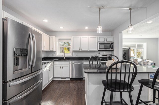 kitchen with appliances with stainless steel finishes, hanging light fixtures, white cabinetry, and a wealth of natural light