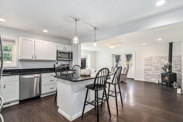 kitchen with a breakfast bar, a wood stove, white cabinets, appliances with stainless steel finishes, and a center island