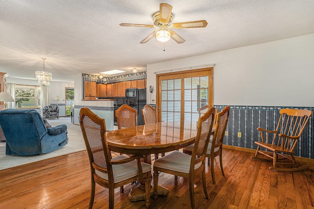 dining area with light hardwood / wood-style floors, a textured ceiling, and ceiling fan with notable chandelier