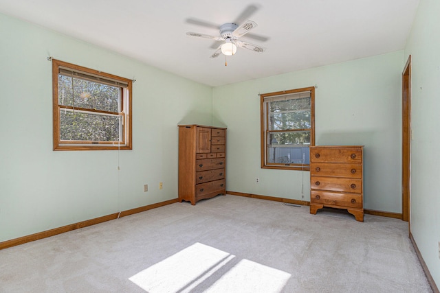 unfurnished bedroom with multiple windows, light colored carpet, and ceiling fan