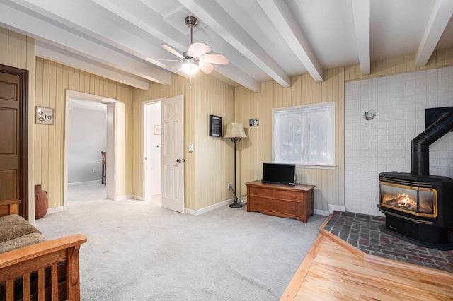 living area featuring a wood stove, beamed ceiling, ceiling fan, and carpet flooring