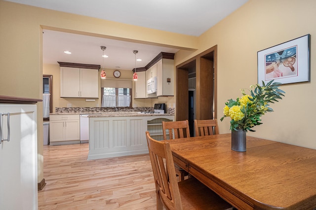 kitchen with white cabinets, white appliances, sink, light hardwood / wood-style floors, and decorative light fixtures