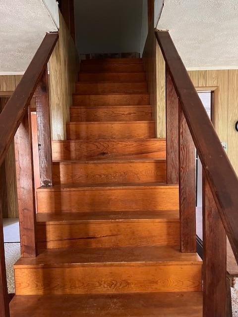 stairway featuring wood walls and a textured ceiling