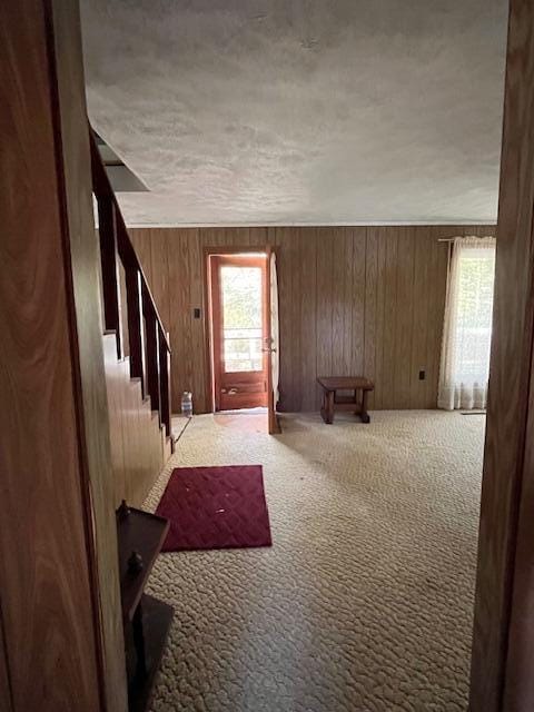 carpeted entryway with wood walls and a textured ceiling