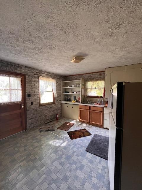 kitchen featuring plenty of natural light, white refrigerator, brick wall, and a textured ceiling