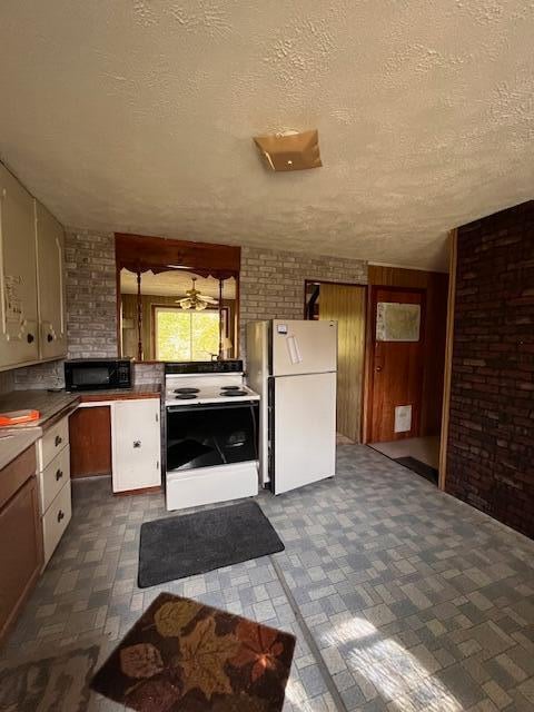 kitchen with white appliances, brick wall, and a textured ceiling