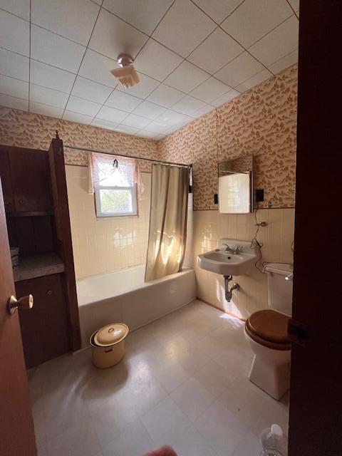 full bathroom with shower / bath combination with curtain, tile walls, toilet, and sink