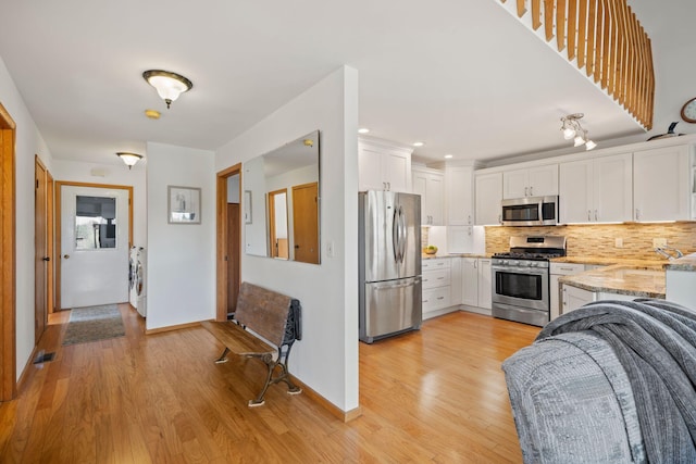 kitchen featuring white cabinets, tasteful backsplash, washer / clothes dryer, appliances with stainless steel finishes, and light hardwood / wood-style floors