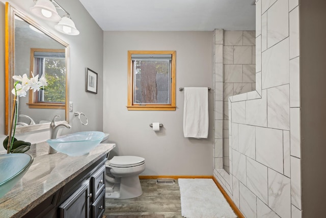 bathroom with wood-type flooring, vanity, toilet, and tiled shower