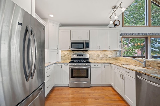 kitchen with light hardwood / wood-style flooring, sink, light stone countertops, white cabinets, and appliances with stainless steel finishes