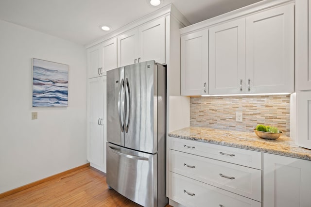 kitchen with light stone countertops, white cabinets, stainless steel fridge, and light wood-type flooring