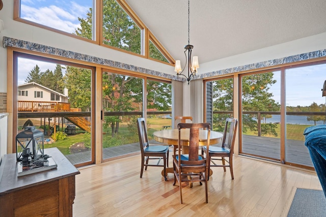 dining room featuring light wood-type flooring, high vaulted ceiling, a notable chandelier, and a wealth of natural light