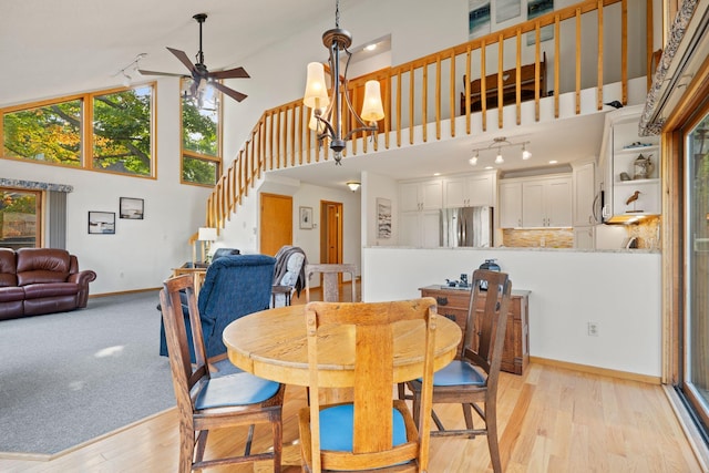 dining space featuring ceiling fan with notable chandelier, light wood-type flooring, and a high ceiling