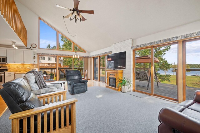 carpeted living room featuring ceiling fan with notable chandelier, high vaulted ceiling, and a fireplace