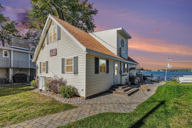 back house at dusk featuring a lawn and a water view