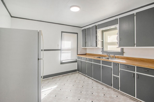 kitchen featuring wooden counters, sink, white fridge, and gray cabinetry