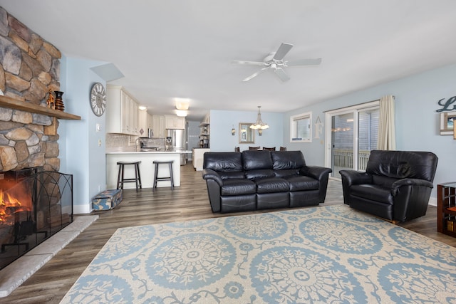 living room featuring a stone fireplace, ceiling fan with notable chandelier, and dark hardwood / wood-style flooring