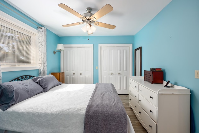 bedroom with two closets, wood-type flooring, and ceiling fan