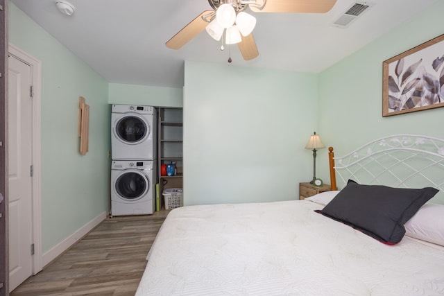 bedroom featuring stacked washing maching and dryer, hardwood / wood-style floors, and ceiling fan