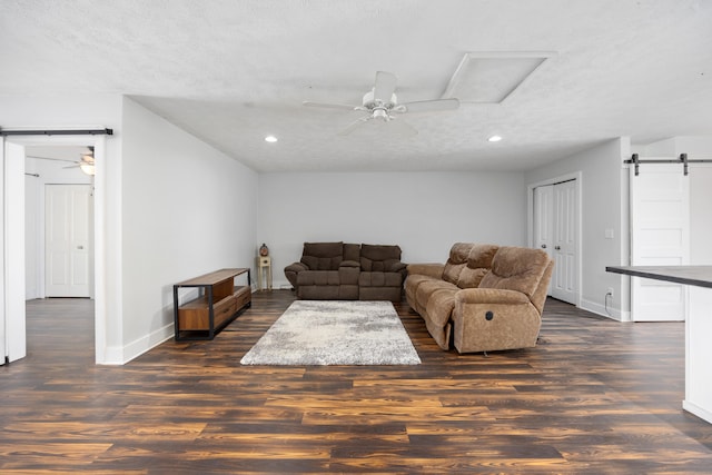 living room with dark wood-type flooring, a barn door, a textured ceiling, and ceiling fan