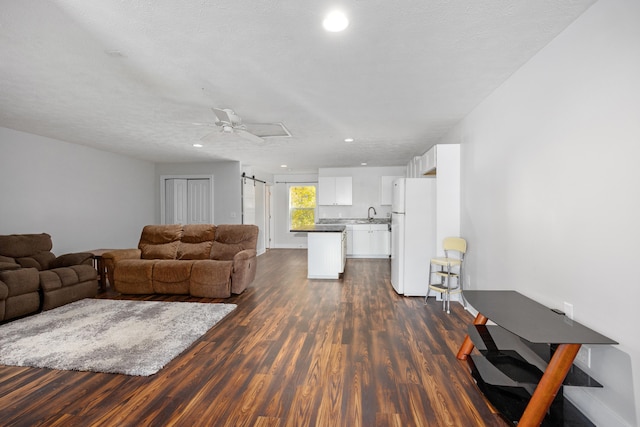 living room featuring a barn door, a textured ceiling, dark hardwood / wood-style floors, and ceiling fan