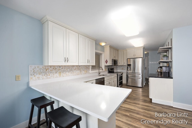 kitchen featuring kitchen peninsula, backsplash, appliances with stainless steel finishes, dark hardwood / wood-style flooring, and sink