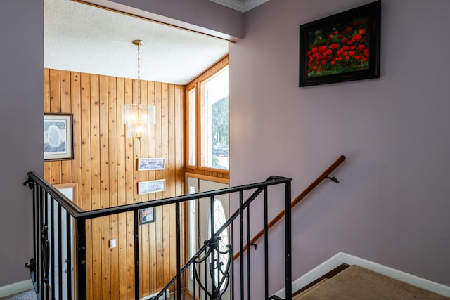 stairs featuring wood walls, carpet floors, and an inviting chandelier