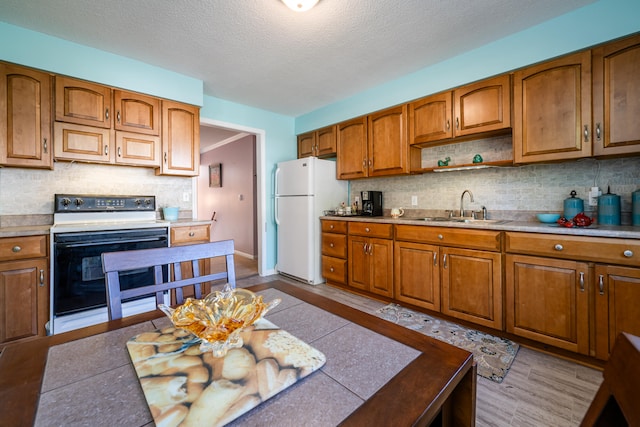 kitchen with white appliances, sink, a textured ceiling, light hardwood / wood-style floors, and tasteful backsplash