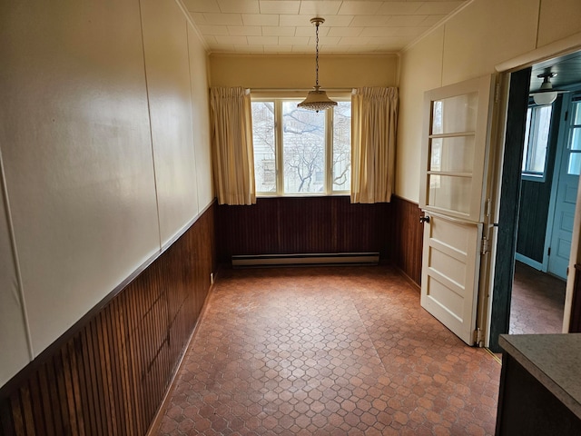 unfurnished dining area with ceiling fan, baseboard heating, wood walls, and ornamental molding