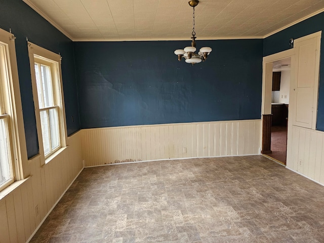 empty room featuring crown molding, wooden walls, and an inviting chandelier