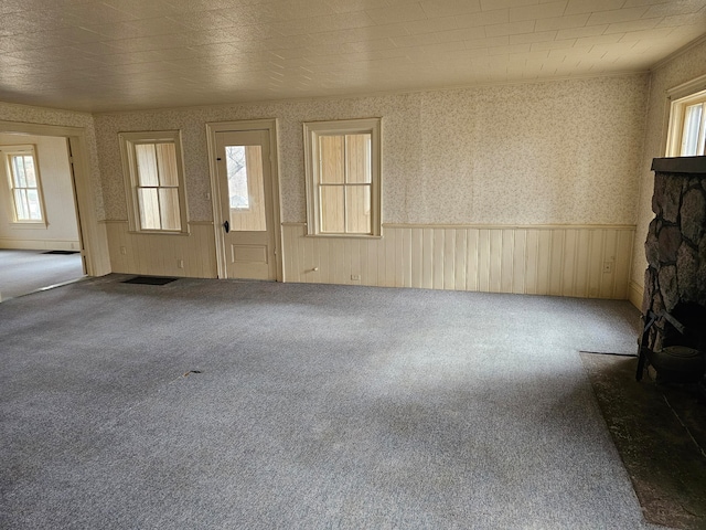 unfurnished living room featuring a wealth of natural light, a stone fireplace, and carpet flooring