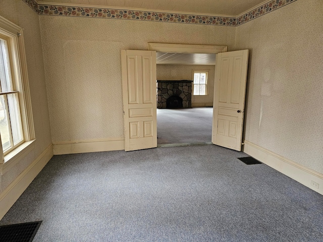 carpeted spare room with a stone fireplace, ornamental molding, and a healthy amount of sunlight