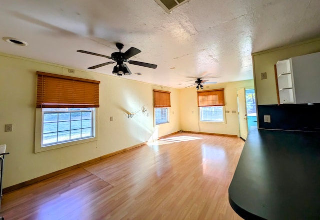 unfurnished living room with light hardwood / wood-style floors, a textured ceiling, and a wealth of natural light