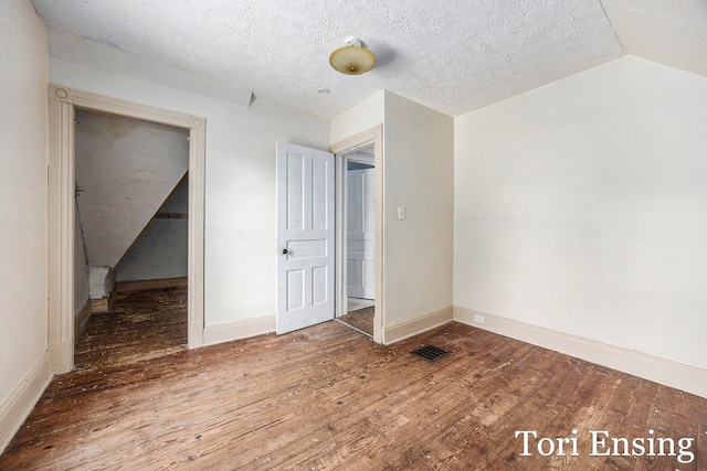 spare room with hardwood / wood-style floors, vaulted ceiling, and a textured ceiling