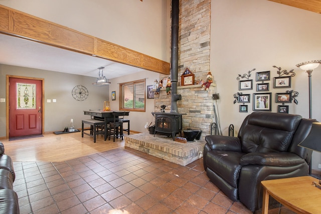 living room with a towering ceiling, beam ceiling, hardwood / wood-style flooring, and a wood stove