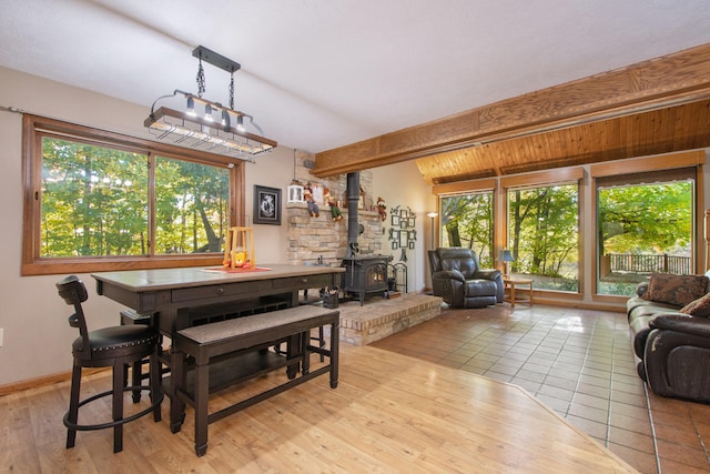 dining space featuring a wood stove, lofted ceiling with beams, and light tile patterned floors