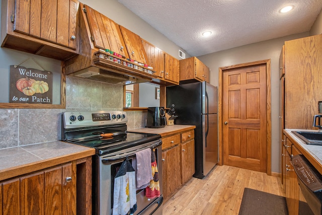 kitchen with sink, a textured ceiling, light hardwood / wood-style floors, stainless steel appliances, and decorative backsplash