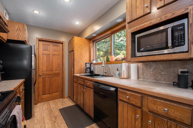 kitchen featuring decorative backsplash, tile counters, sink, black appliances, and light wood-type flooring