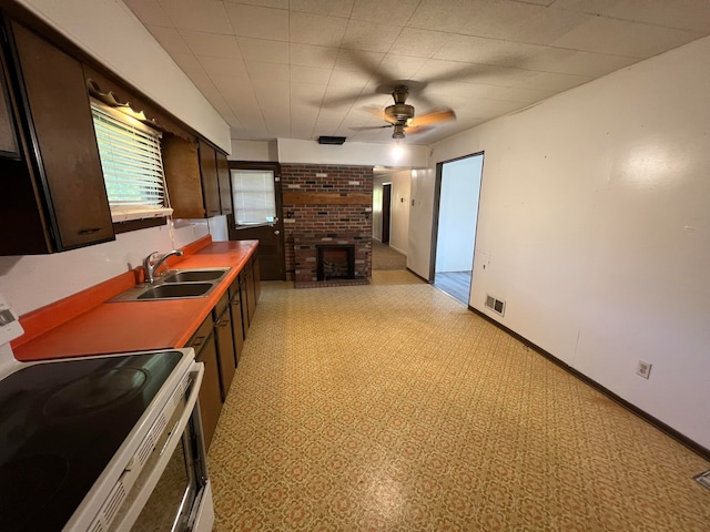 kitchen with white range, sink, dark brown cabinetry, a brick fireplace, and ceiling fan