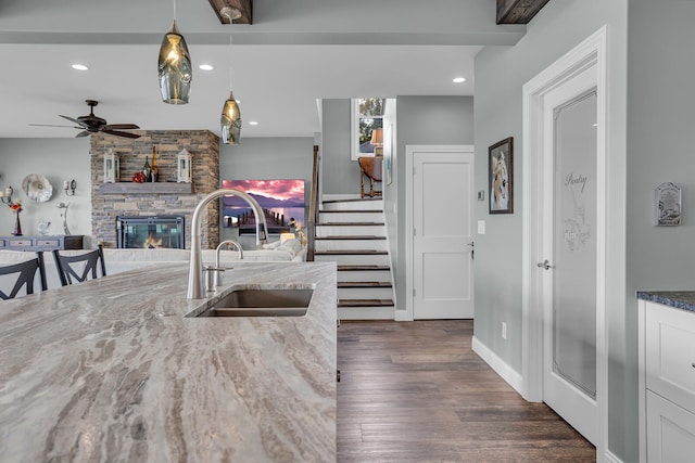 kitchen featuring dark wood-type flooring, dark stone counters, sink, decorative light fixtures, and a fireplace