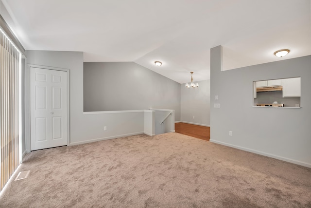 carpeted empty room with a chandelier and vaulted ceiling