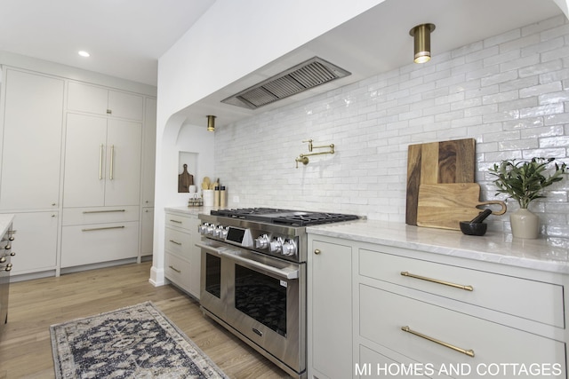 kitchen with decorative backsplash, white cabinetry, stainless steel stove, light hardwood / wood-style flooring, and range hood