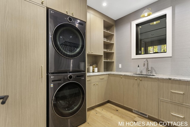 washroom featuring light hardwood / wood-style flooring, stacked washer / dryer, cabinets, and sink