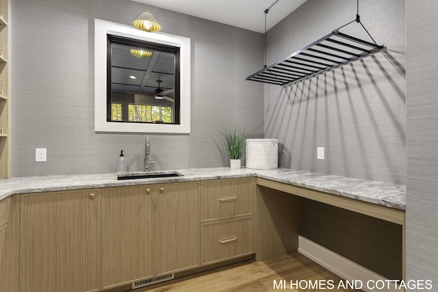 interior space with sink, light hardwood / wood-style flooring, light stone counters, and ceiling fan