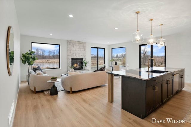 kitchen featuring sink, hanging light fixtures, light stone counters, an island with sink, and light wood-type flooring